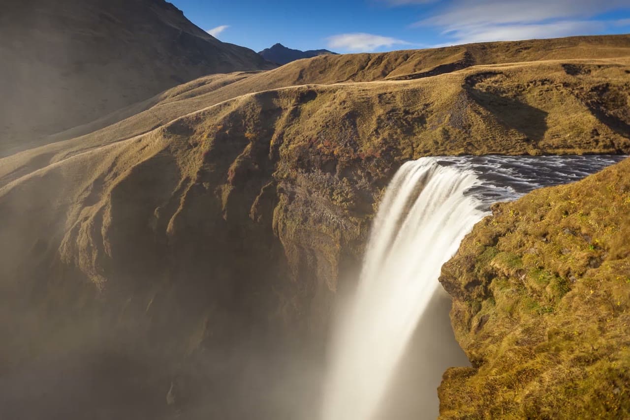 A waterfall pouring off a green clifftop into mist